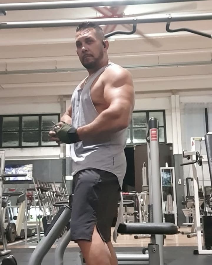 Carlo in sala pesi, di tre quarti, con la canotta grigia e i guanti da allenamento